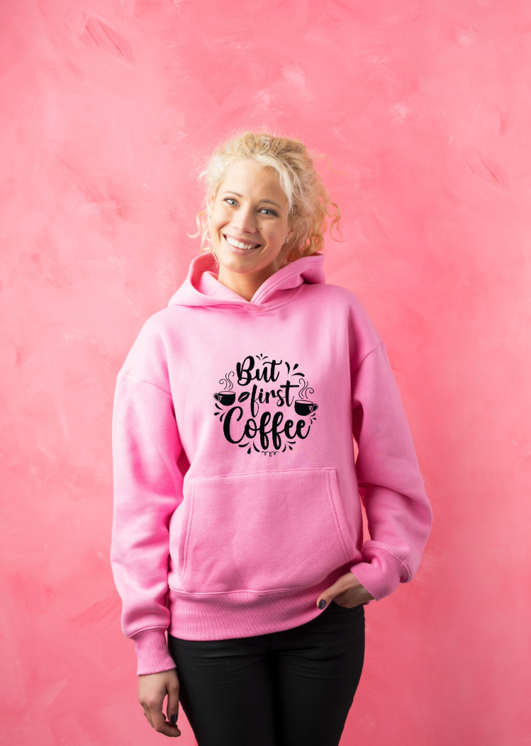 Blonde woman in pink hoodie with 'But first coffee' design Smiling woman in a pink hoodie with 'But first coffee' text and coffee motif, standing in front of a pink wall – customize your hoodie
