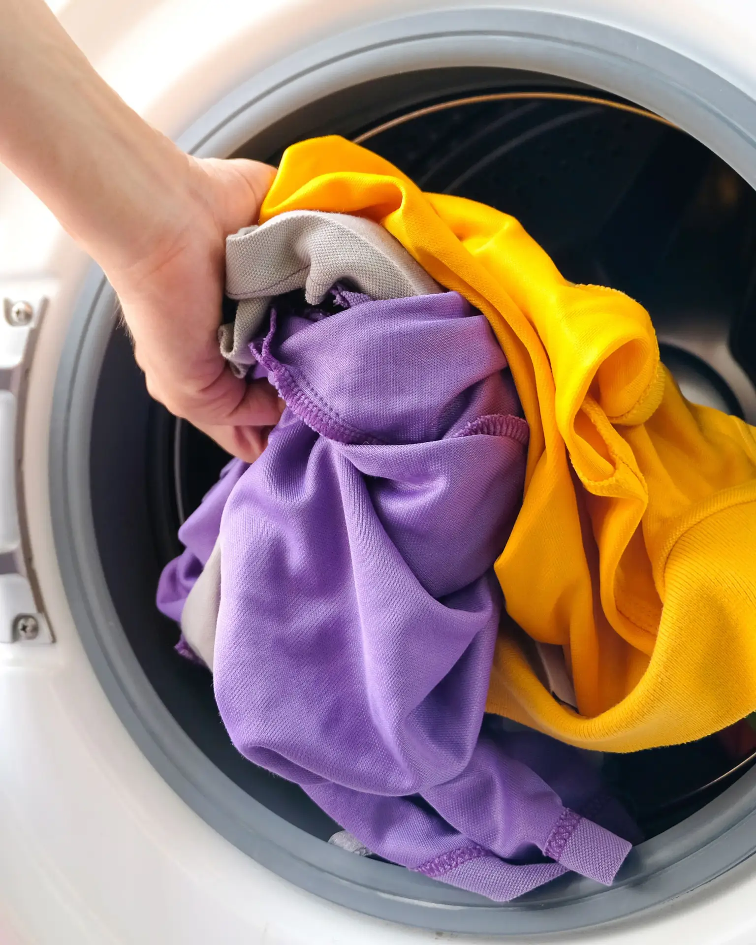 Washing Clothes Properly – Tips for Caring for Printed T-Shirts and Hoodies Man places printed clothes into washing machine – care tip for personalized T-shirts and hoodies