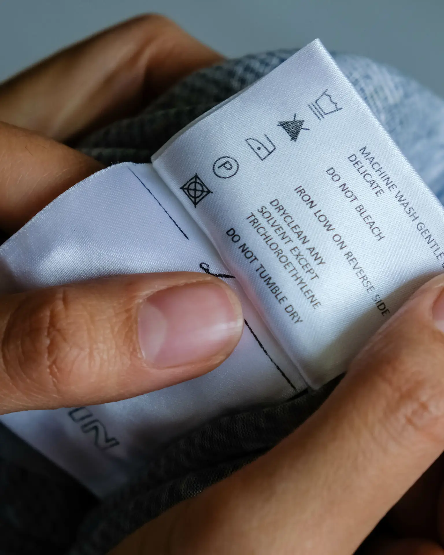 Clothing Care Label Close-Up – Washing Instructions Hands holding a clothing care label with instructions for washing, ironing, and cleaning – textile label close-up