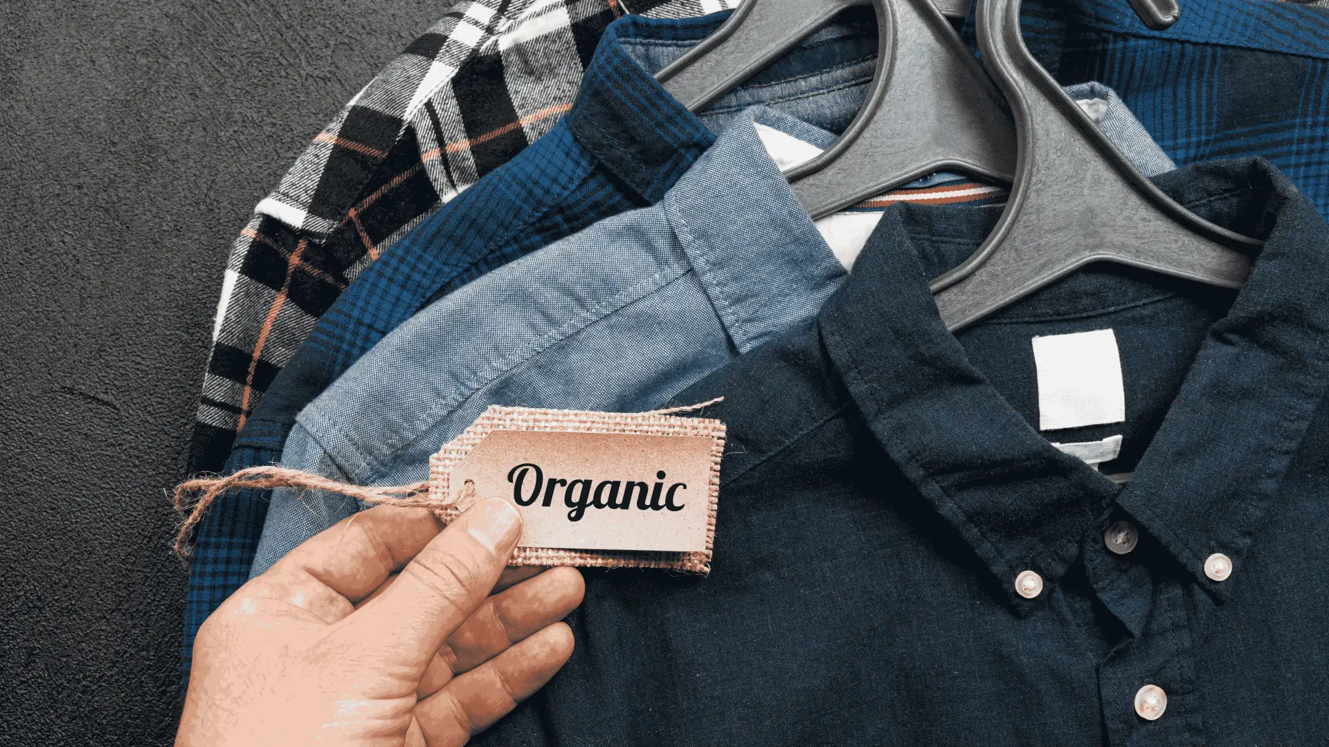 Organic Cotton Shirts on Hangers – Sustainable Fashion Hand holding organic label in front of eco-friendly cotton shirts on hangers – sustainable and ethical clothing choice