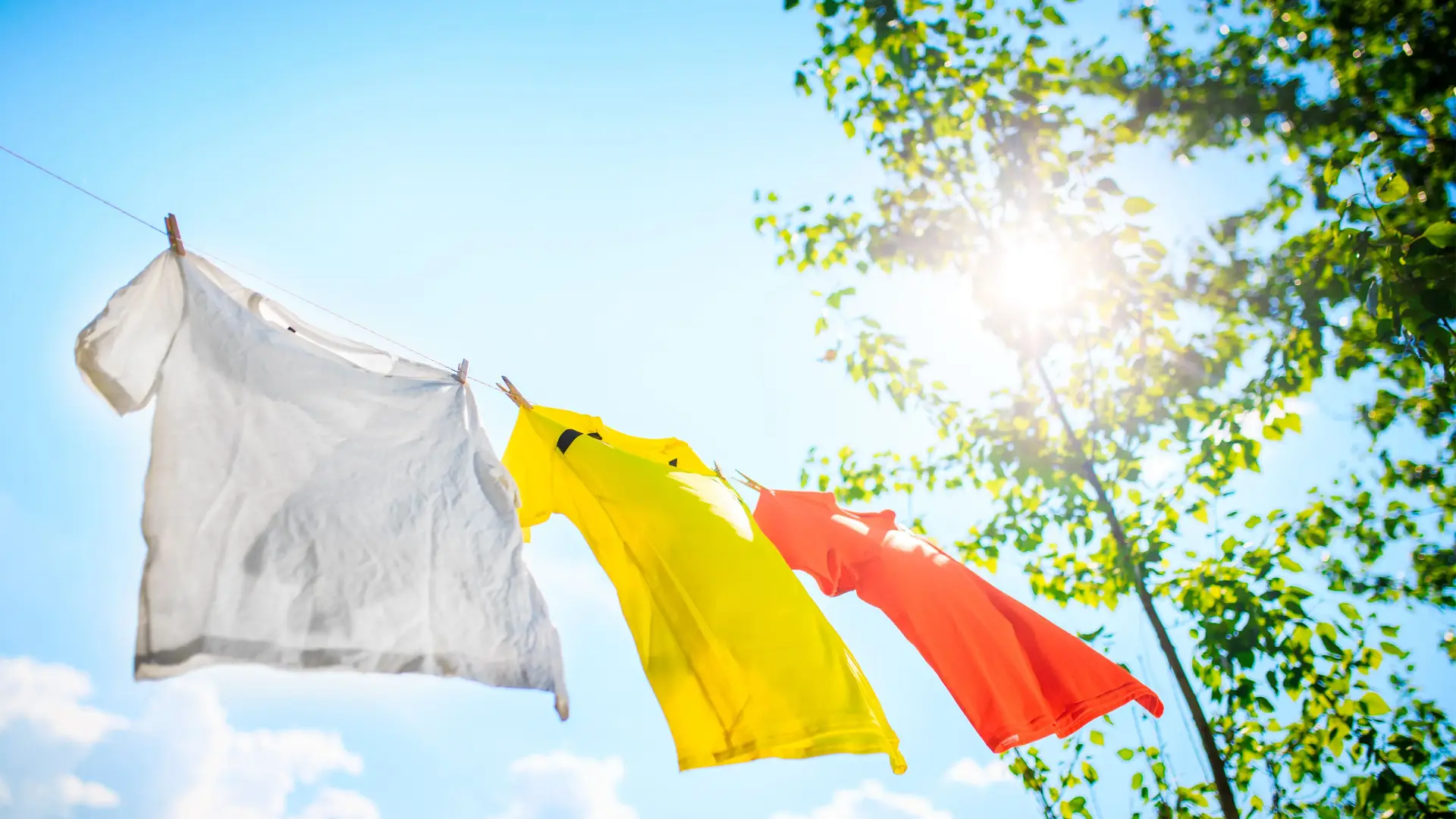 Drying T-Shirts Properly – Air Drying for Printed Shirts and Hoodies Three T-shirts hang on a line under blue sky – gentle drying for personalized clothes