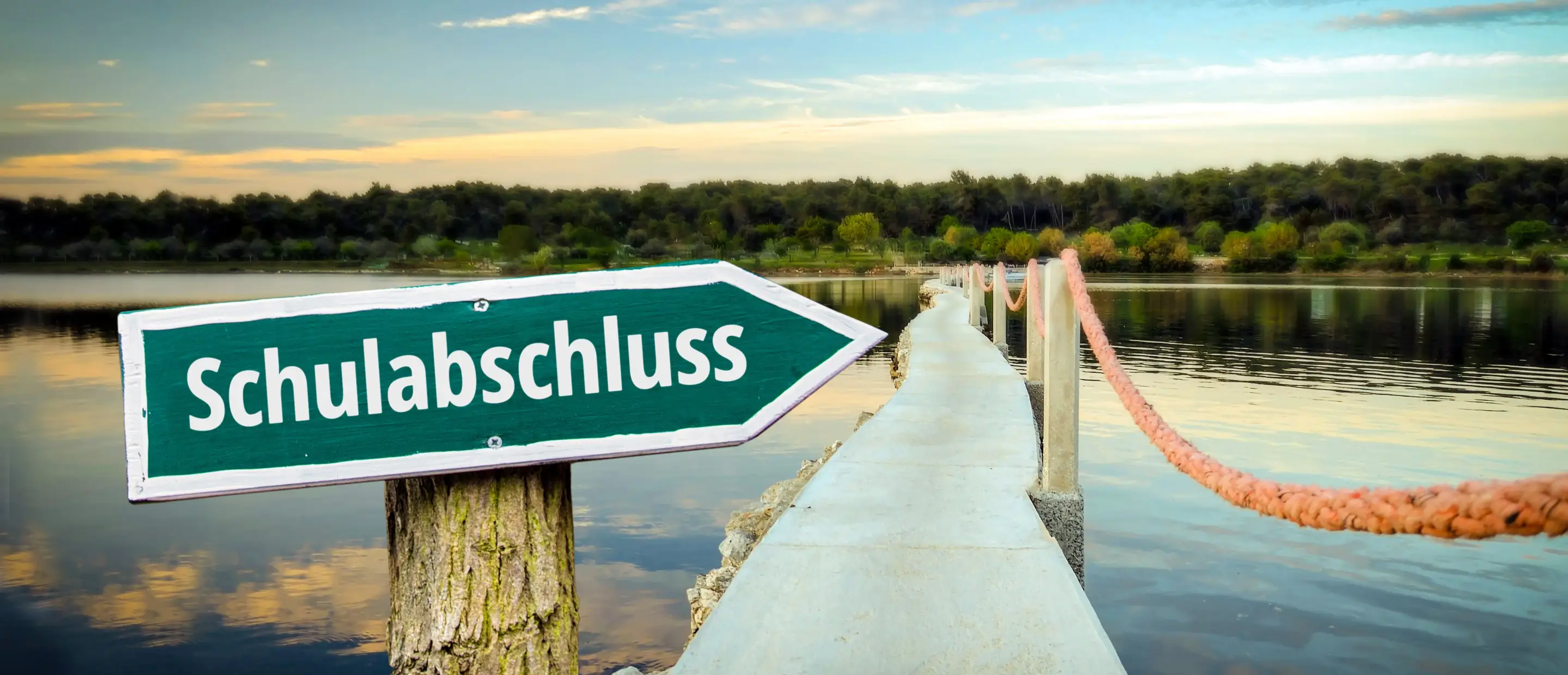 Design your graduation hoodie online: High school graduation hoodie ideas A boardwalk by the lake with a sign saying 'Graduation' in the foreground – symbolic image. Design grad outfits and hoodies online with AI