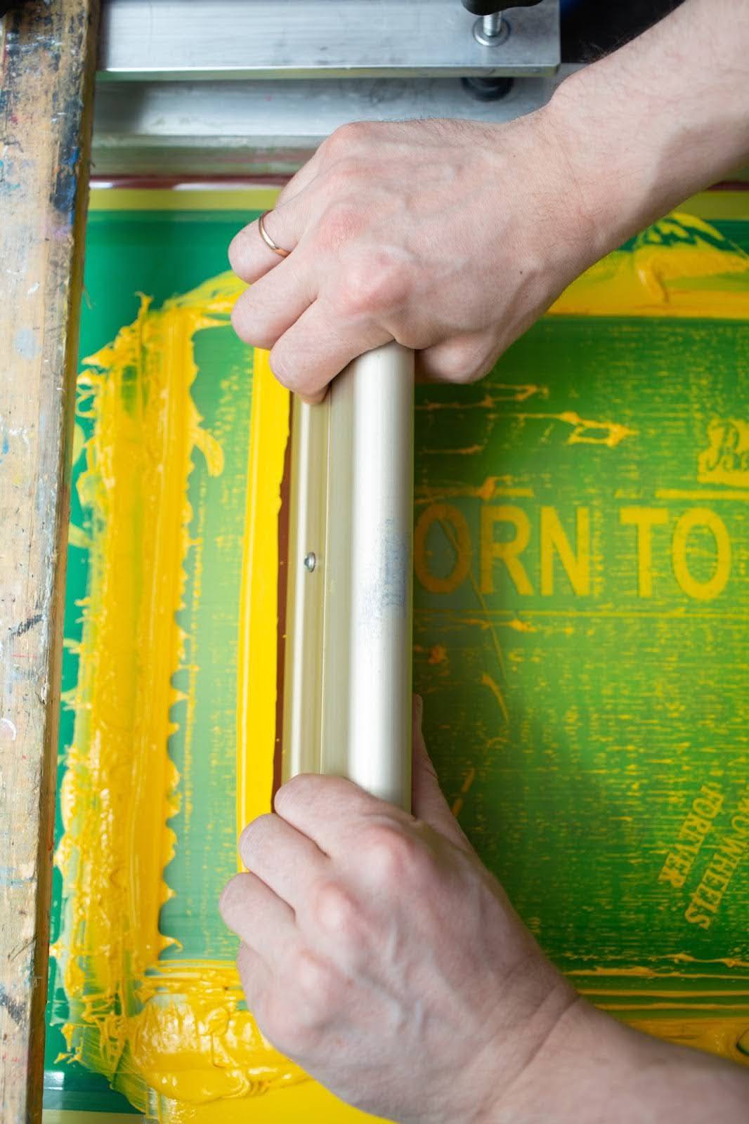 Siebdruckverfahren: Gelbe Farbe wird mithilfe von Schablone und Rakel präzise auf ein T-Shirt in einer Textildruckerei aufgetragen