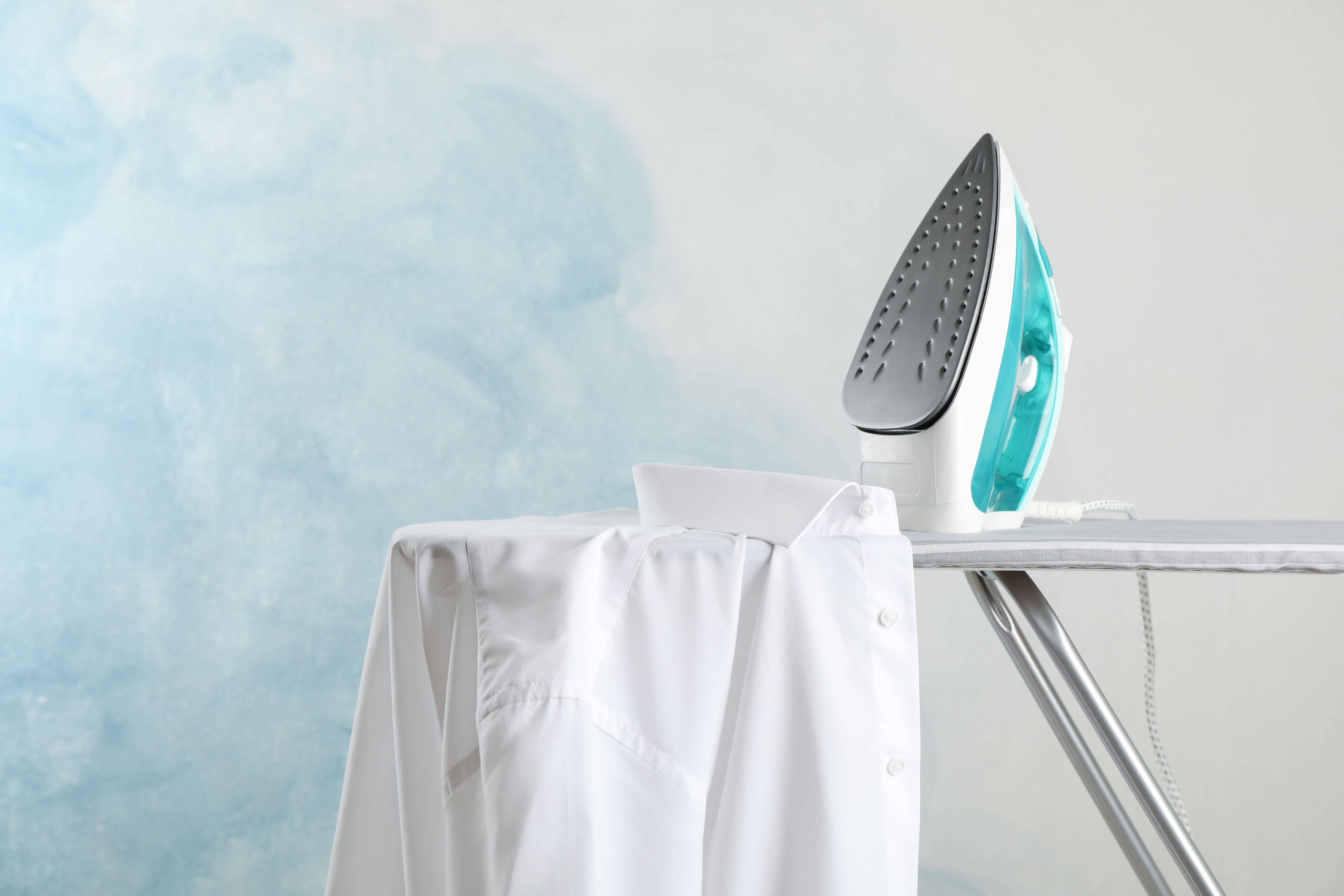 Elektrobügeleisen auf Bügelbrett mit weißem Hemd – ideal zur Fixierung von Transferdruck und Textilfarben auf T-Shirts.