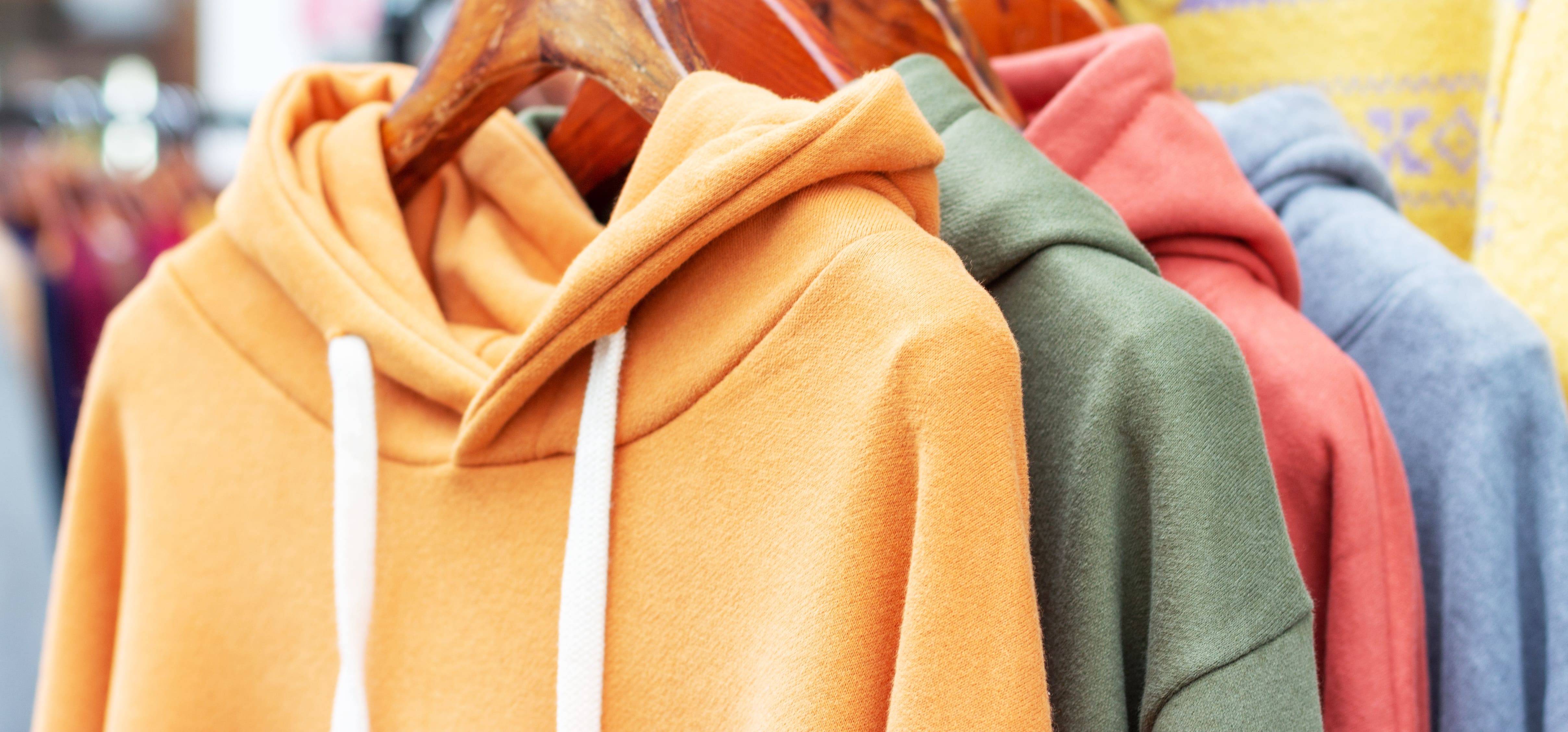 Bunte Sweatshirts auf Kleiderbügeln – farbenfrohe Auswahl an Hoodies, Pullovern und Sweatern im Detail.